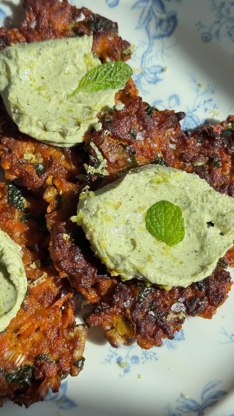 Vegetable fritters topped with green creamy sauce and fresh mint leaves on a floral plate.
