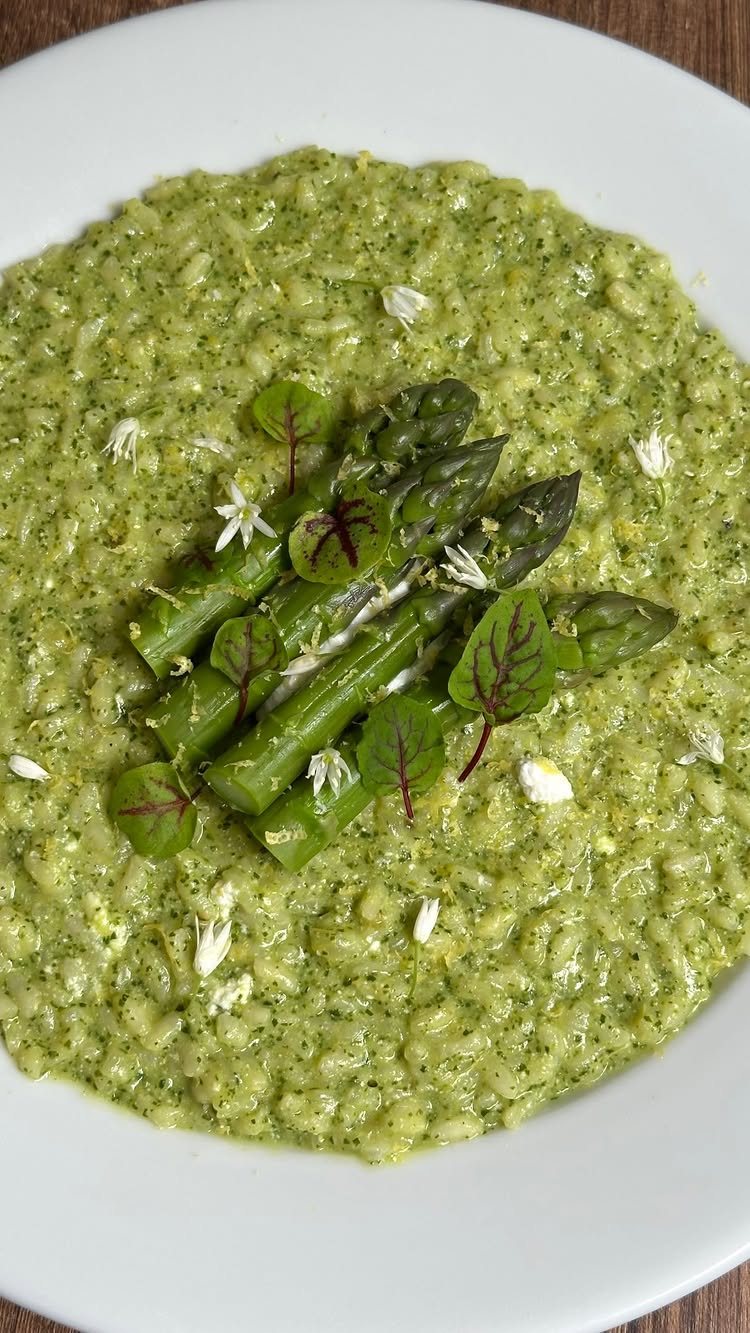 Green asparagus risotto topped with small edible flowers and red-veined microgreens on a white plate.