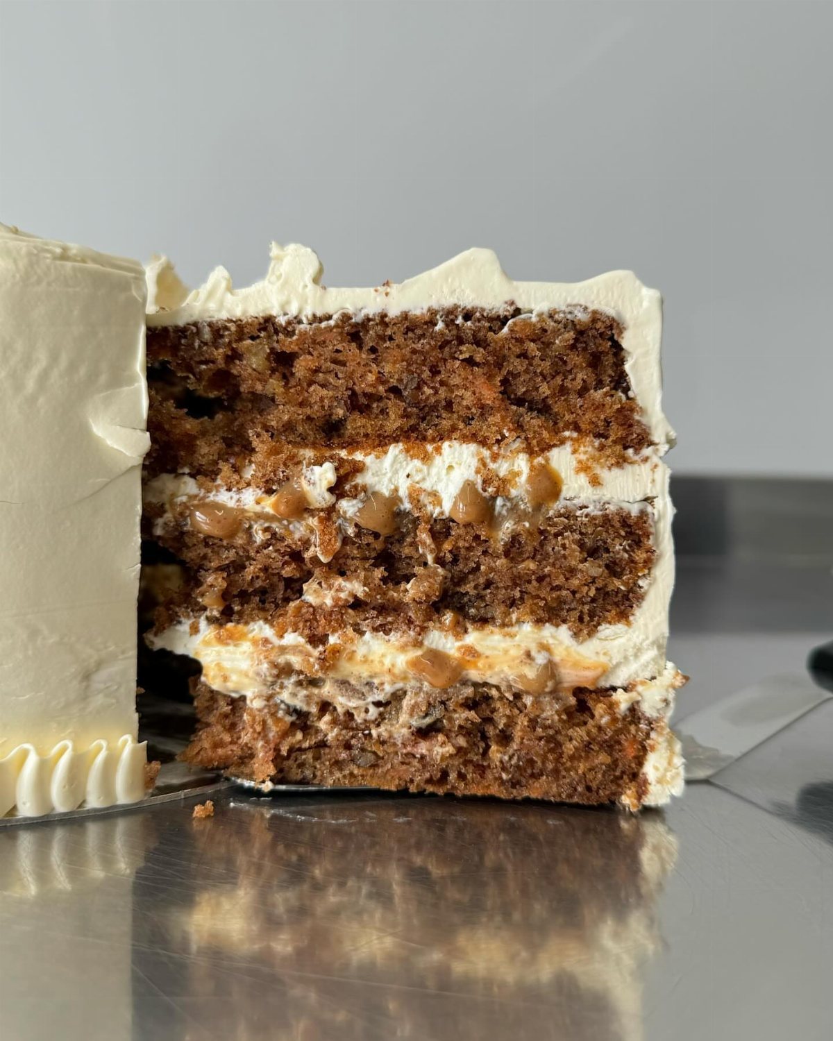 A slice of layered brown cake with white frosting and nut pieces on a metal tray.
