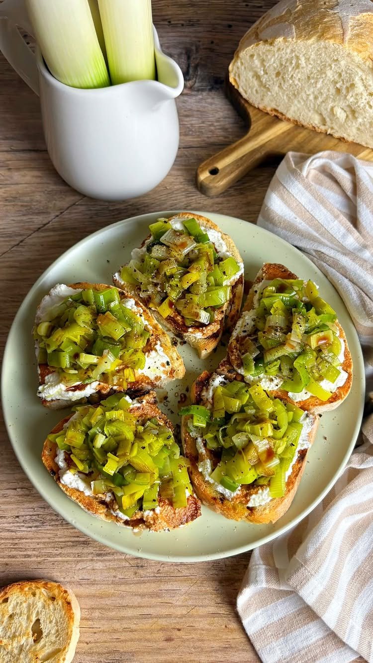 Toasted bread slices topped with creamy cheese and sautéed leeks on a light green plate.