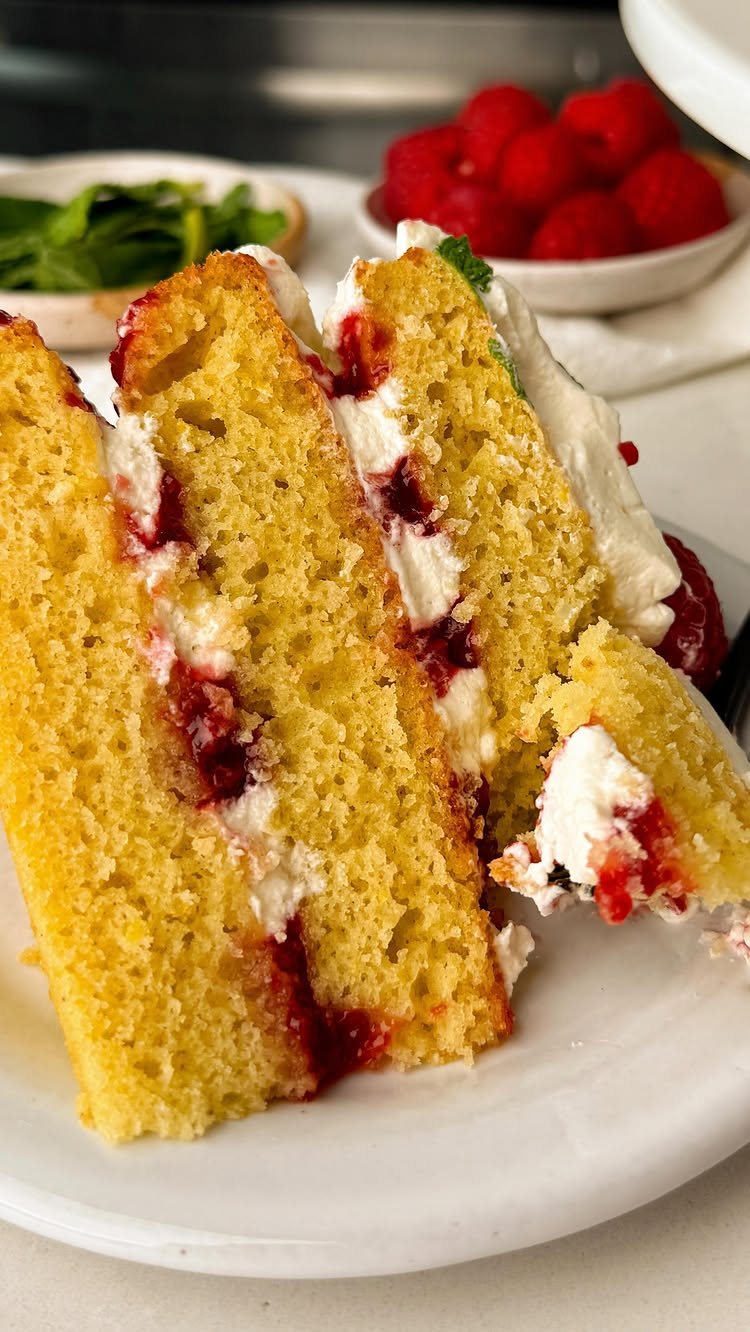 Slices of yellow sponge cake with white cream and red jam filling on a white plate.
