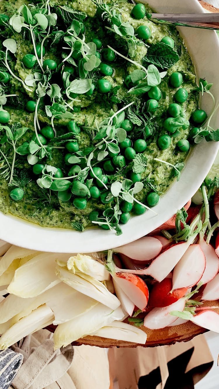 Green pea puree topped with whole peas and microgreens in a white bowl.