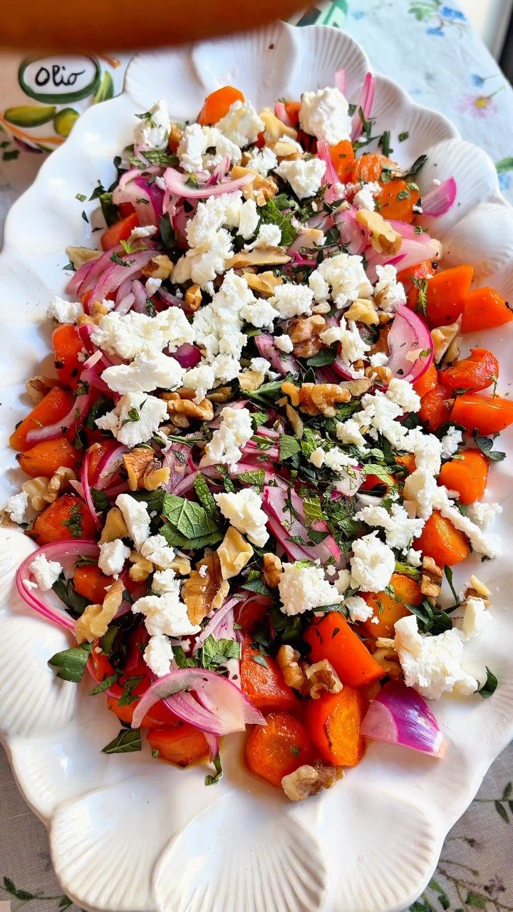 A vibrant spring salad with carrots, red onions, feta cheese, and walnuts on a white platter.