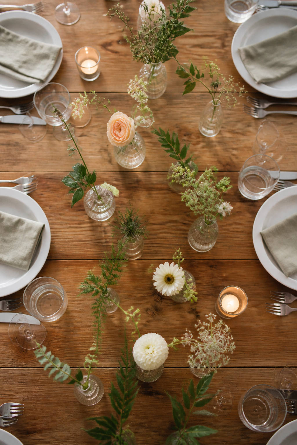 Several small bud vases filled with flowers arranged on a table.