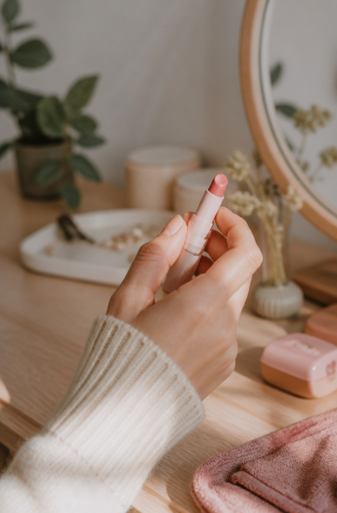 Very Light Makeup: 11 Steps for a Natural 2026 Routine 10 A hand applying tinted lip balm in a softly lit, cozy setting.