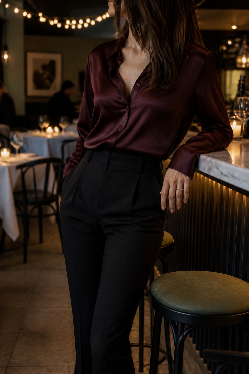 A silk blouse tucked into black trousers, styled at a bar counter.