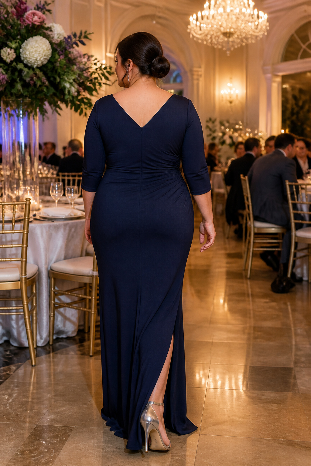 A model showcasing a plus size long cocktail dress in a banquet hall.