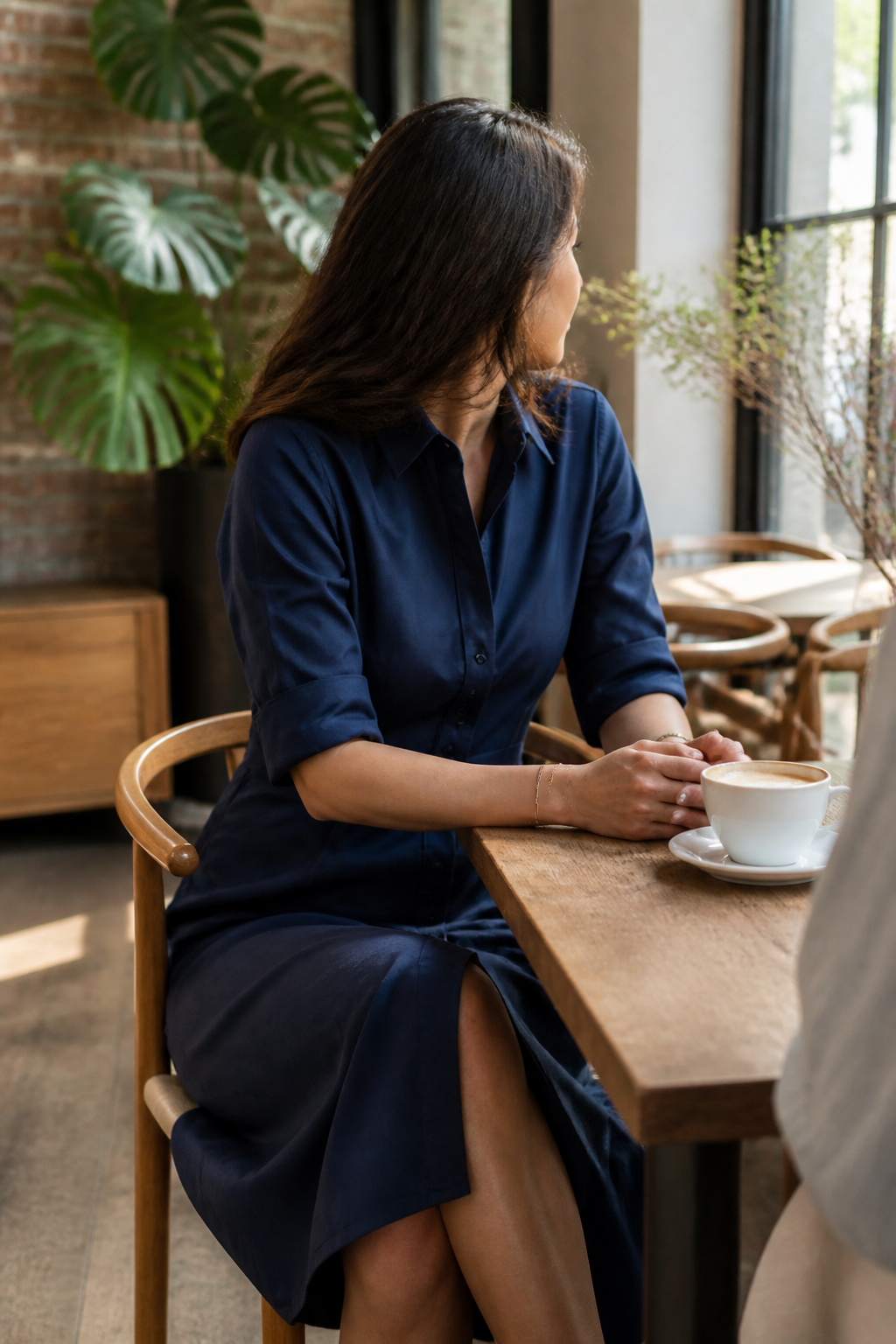 A woman in a button-down shirt dress seated at a café table.