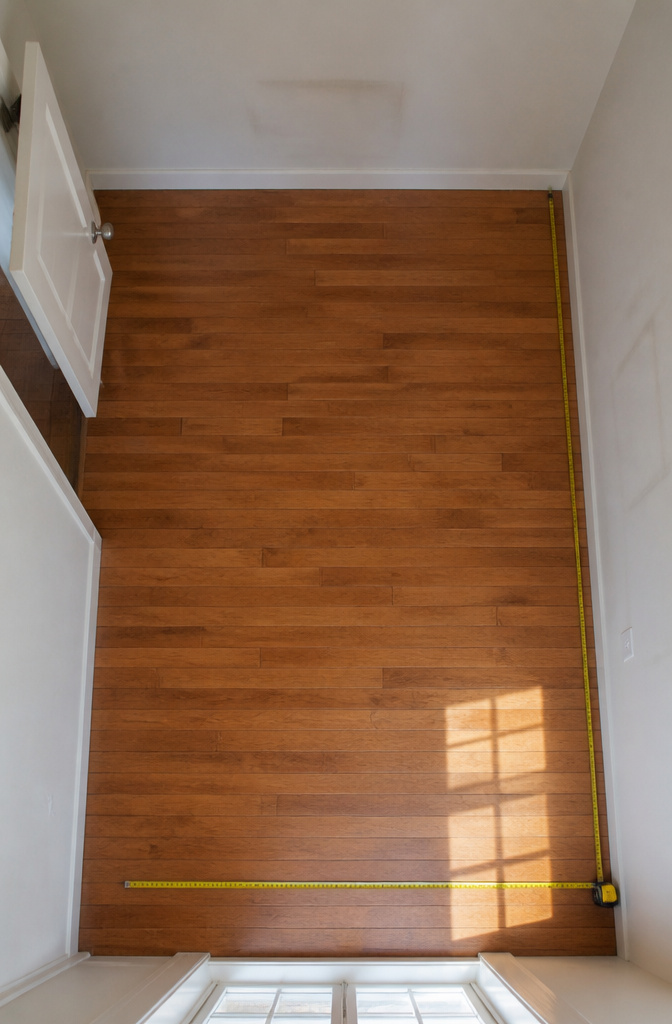 A person measuring a room with a tape measure for a closet conversion.