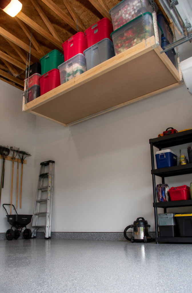 Overhead storage rack in a garage holding plastic storage bins.