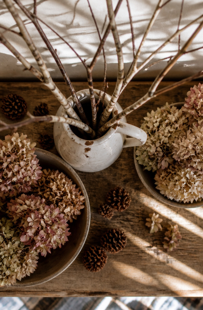 Branches and dried hydrangeas displayed in a pitcher on a mantel.