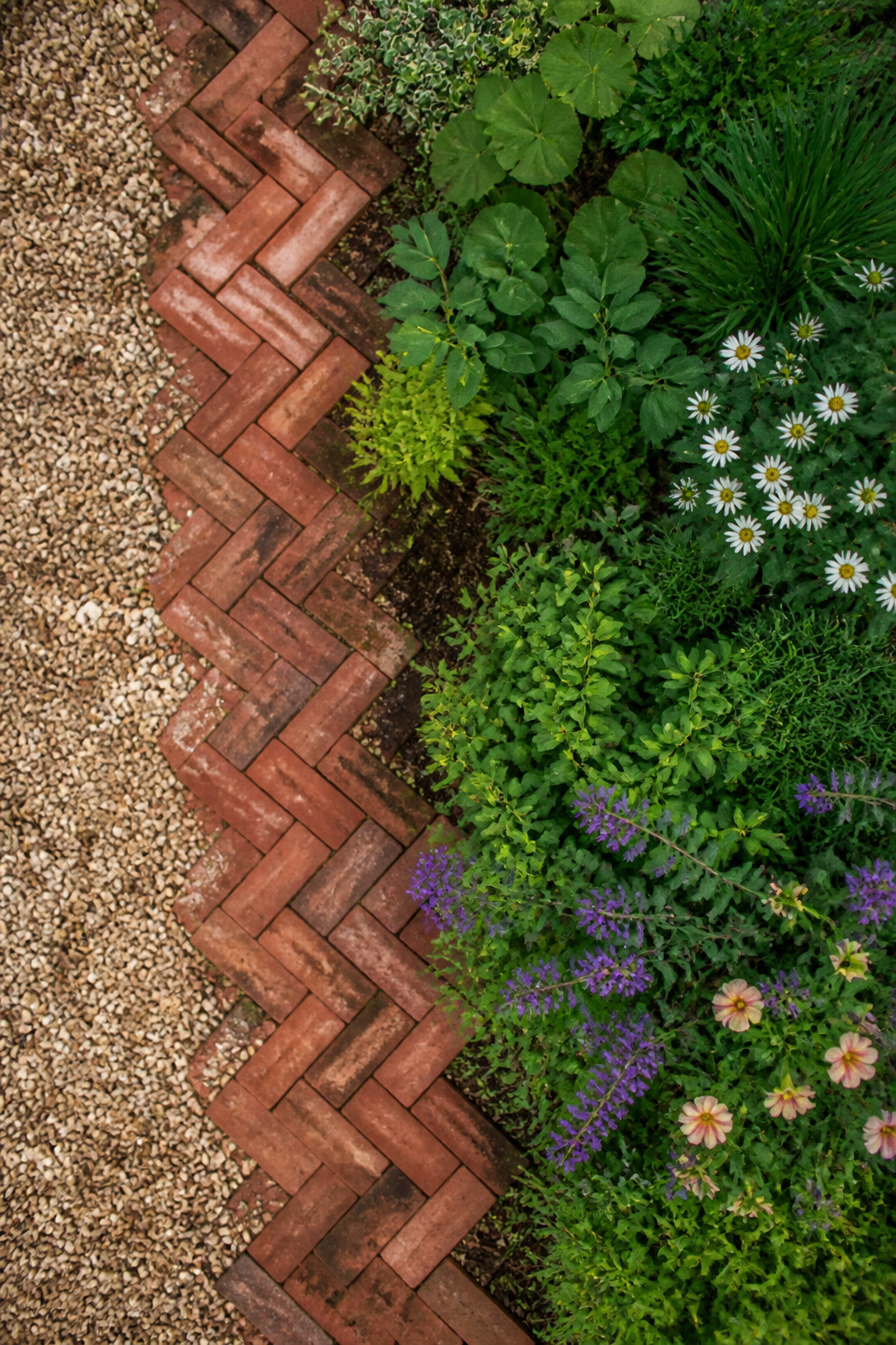 23 Brick and Rock Edging Ideas for Garden Borders (2026) 12 Diagonal herringbone brick pattern along a flowerbed.