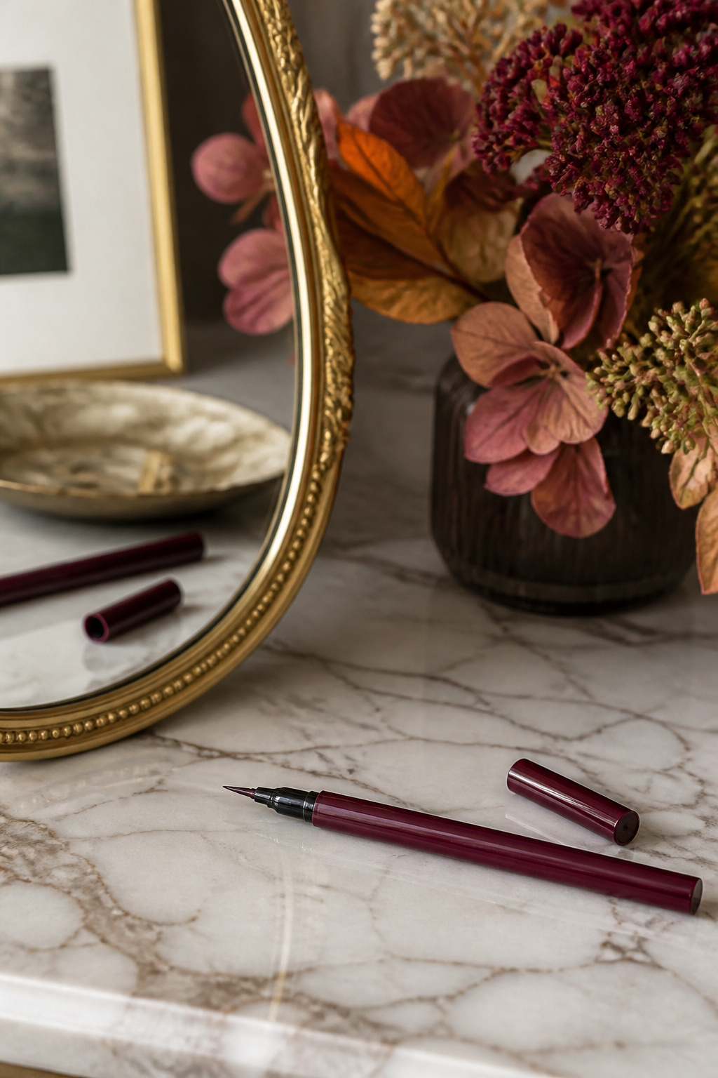Fine-tipped burgundy eyeliner on a marble countertop with autumn flowers.