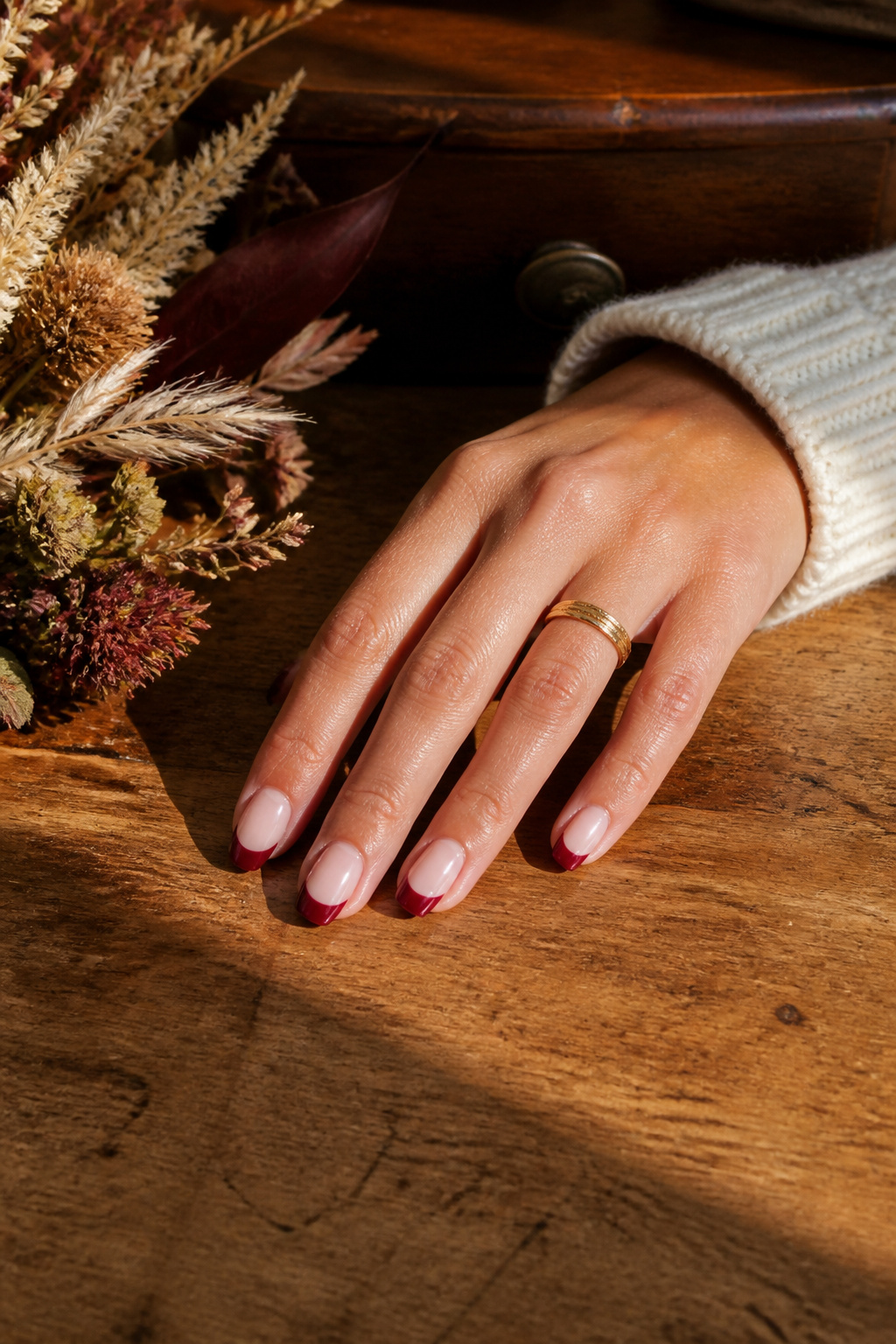 20 Fall Nail Ideas for 2026: Colors, Shapes & Textures 5 Hand with cherry red French tips resting on a wooden desk.