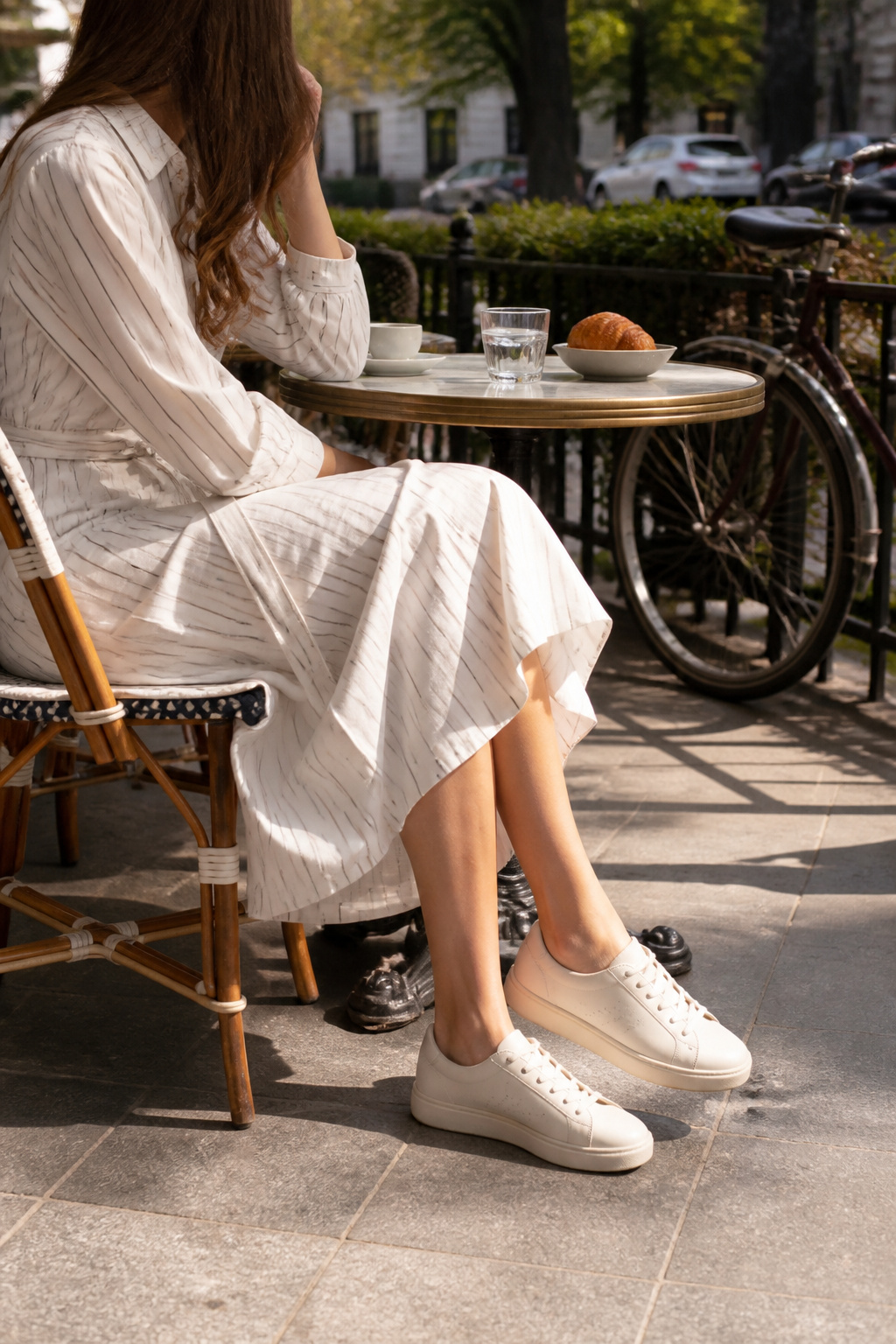 Cole Haan GrandPro sneakers displayed near a model in a shirt dress at a café.
