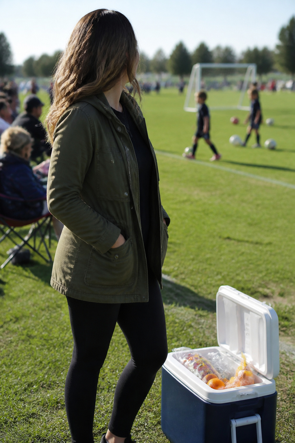 Woman in a utility jacket and leggings on a soccer field.