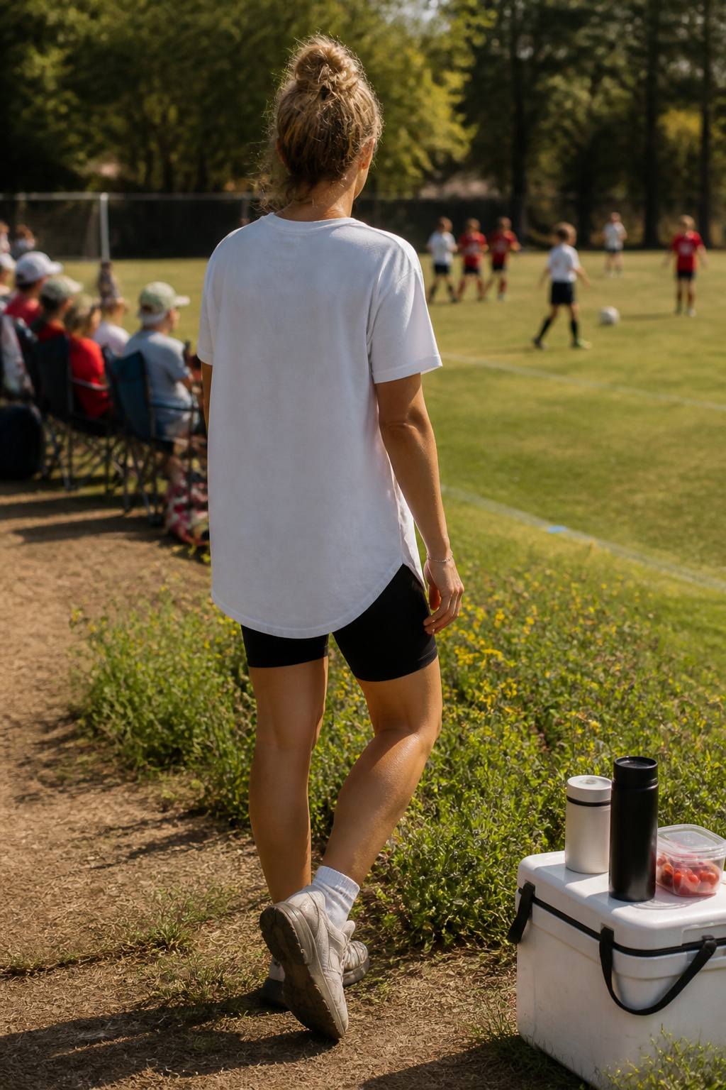 Woman in oversized white tee and black biker shorts at a soccer game.