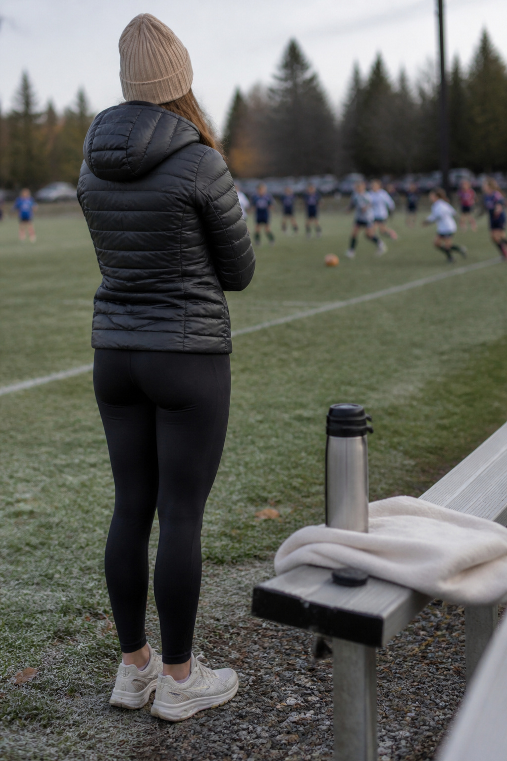 Woman wearing a puffer jacket and leggings on a soccer field.