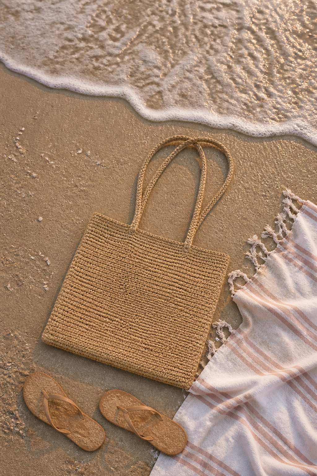 A raffia tote bag positioned on a sandy beach.