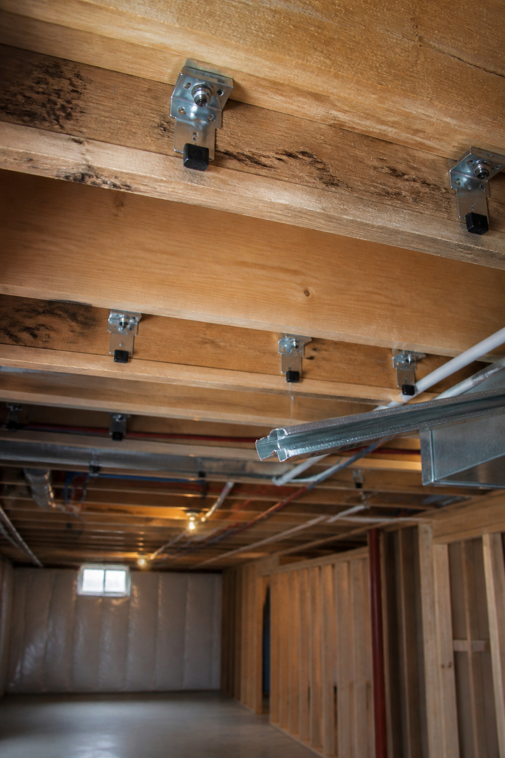 Metal sound isolation clips mounted on wooden joists in a basement.