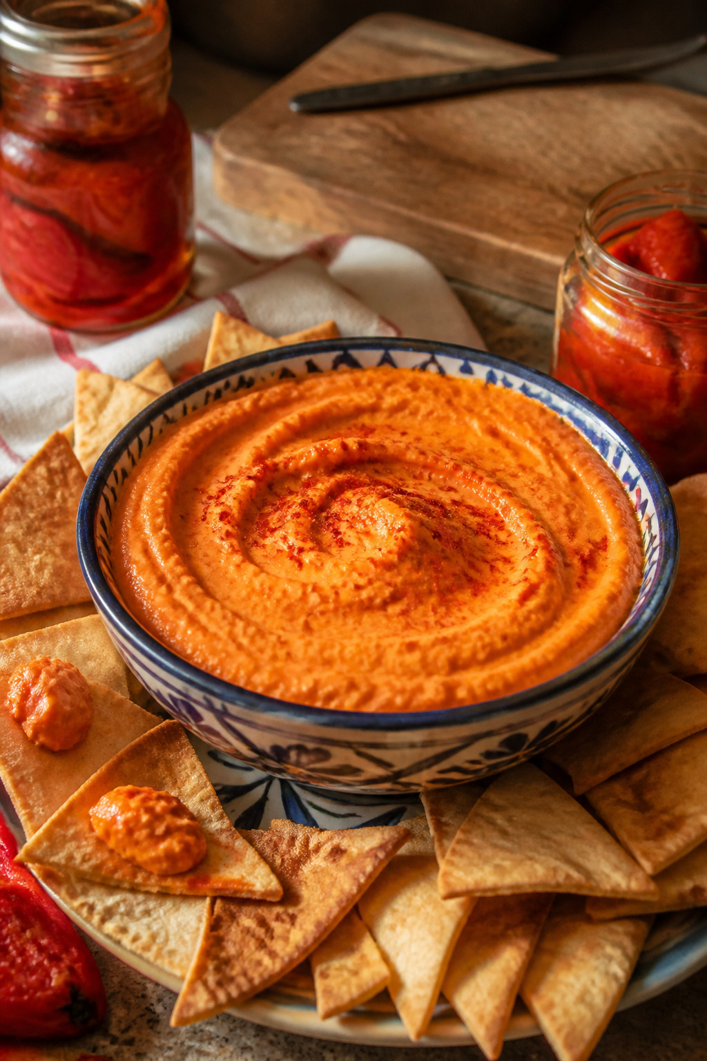 A bowl of roasted red pepper hummus with pita chips.
