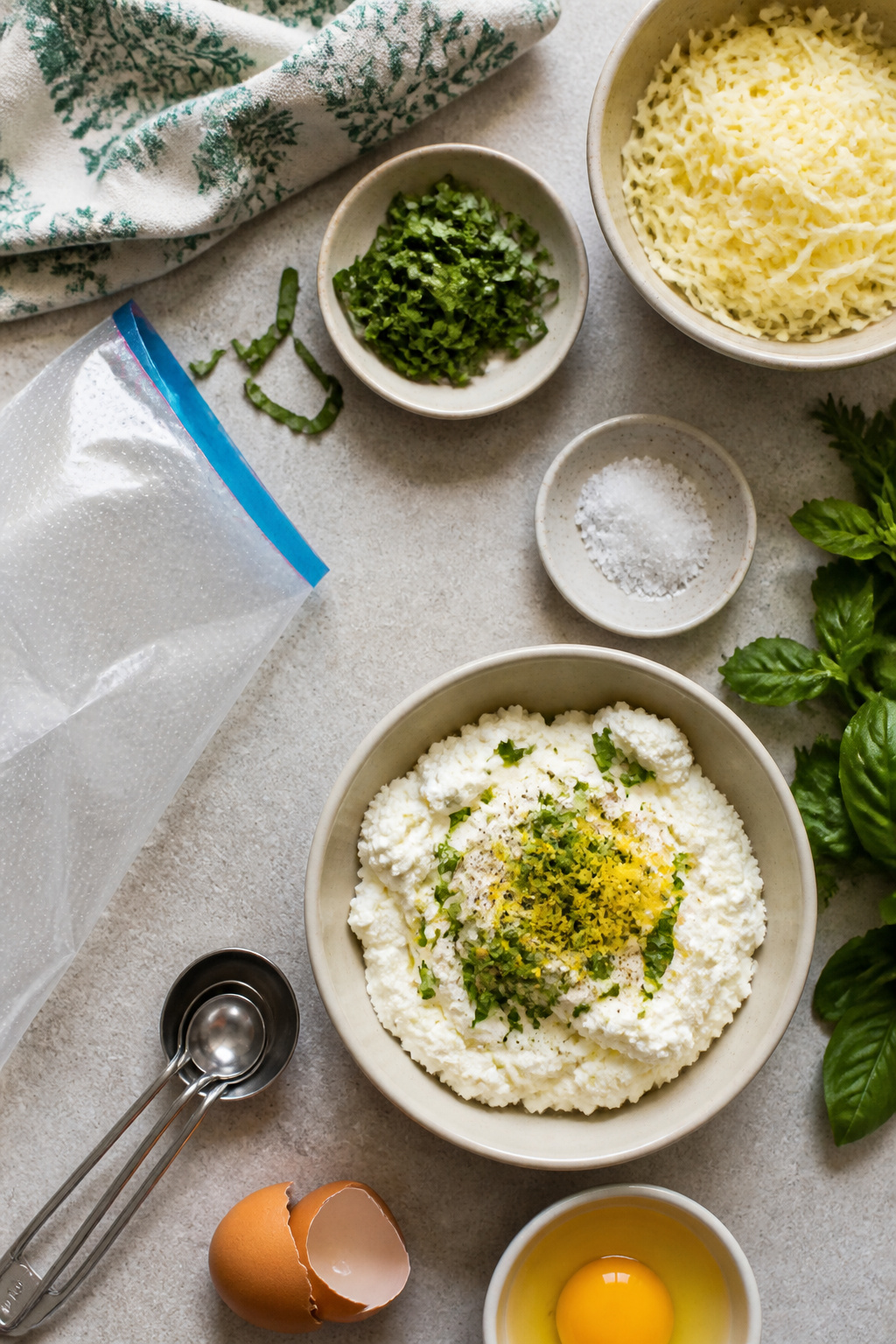 A glass bowl filled with ricotta and herbs for stuffing zucchini flowers.