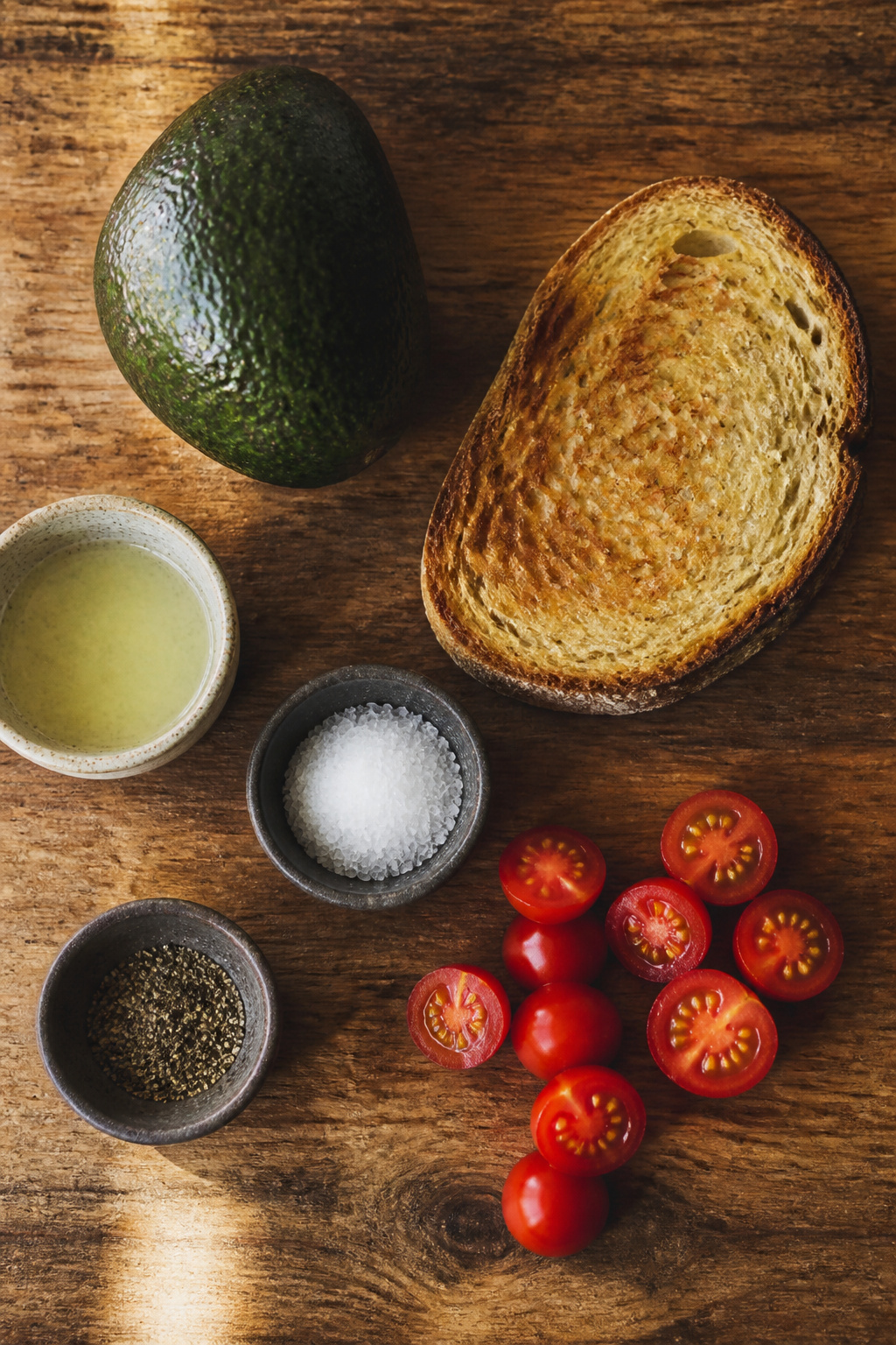 An avocado, bread, and toppings for avocado toast.