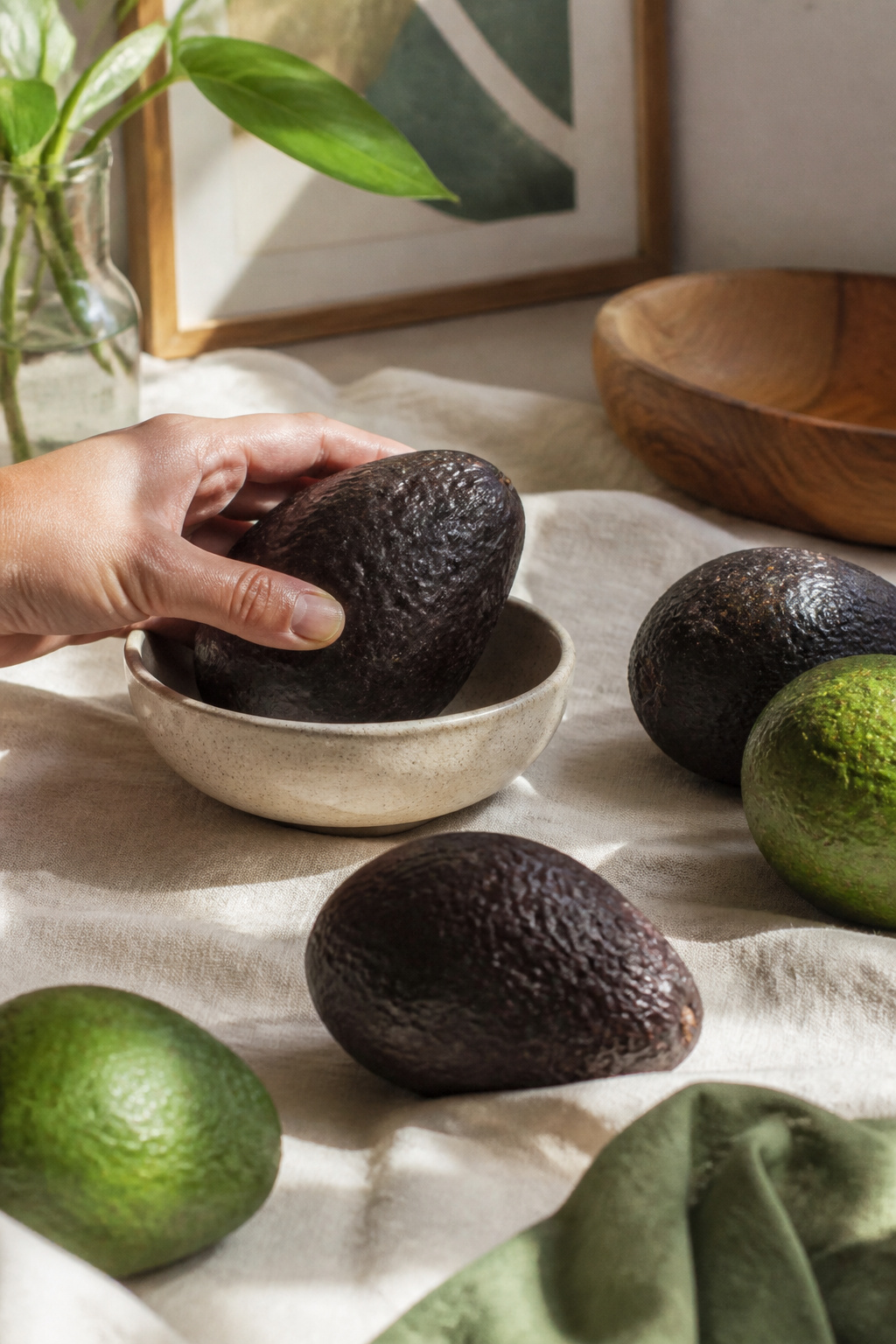 A ripe Hass avocado next to a hand demonstrating its softness.