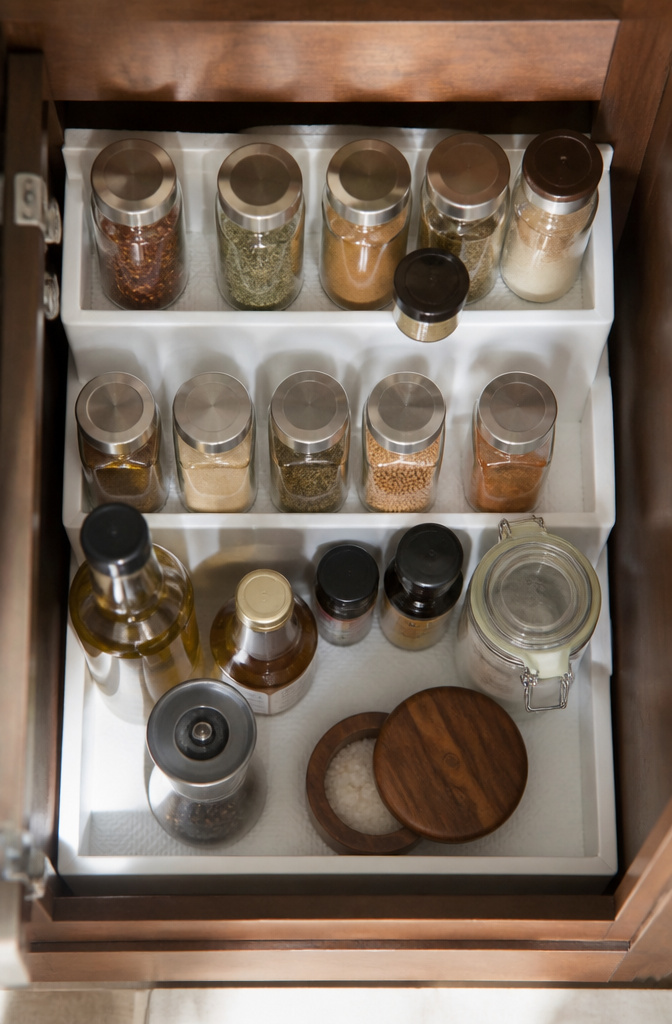 Three-tier shelf organizer holding spice jars in a cabinet.