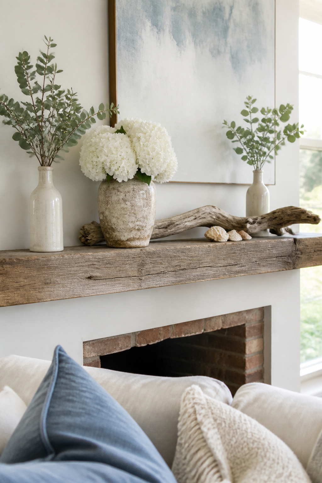 8 Summer Mantel Decorating Ideas for a Fresh, Seasonal Hearth in 2026 1 A mantel with white hydrangeas, eucalyptus branches, and seashells.