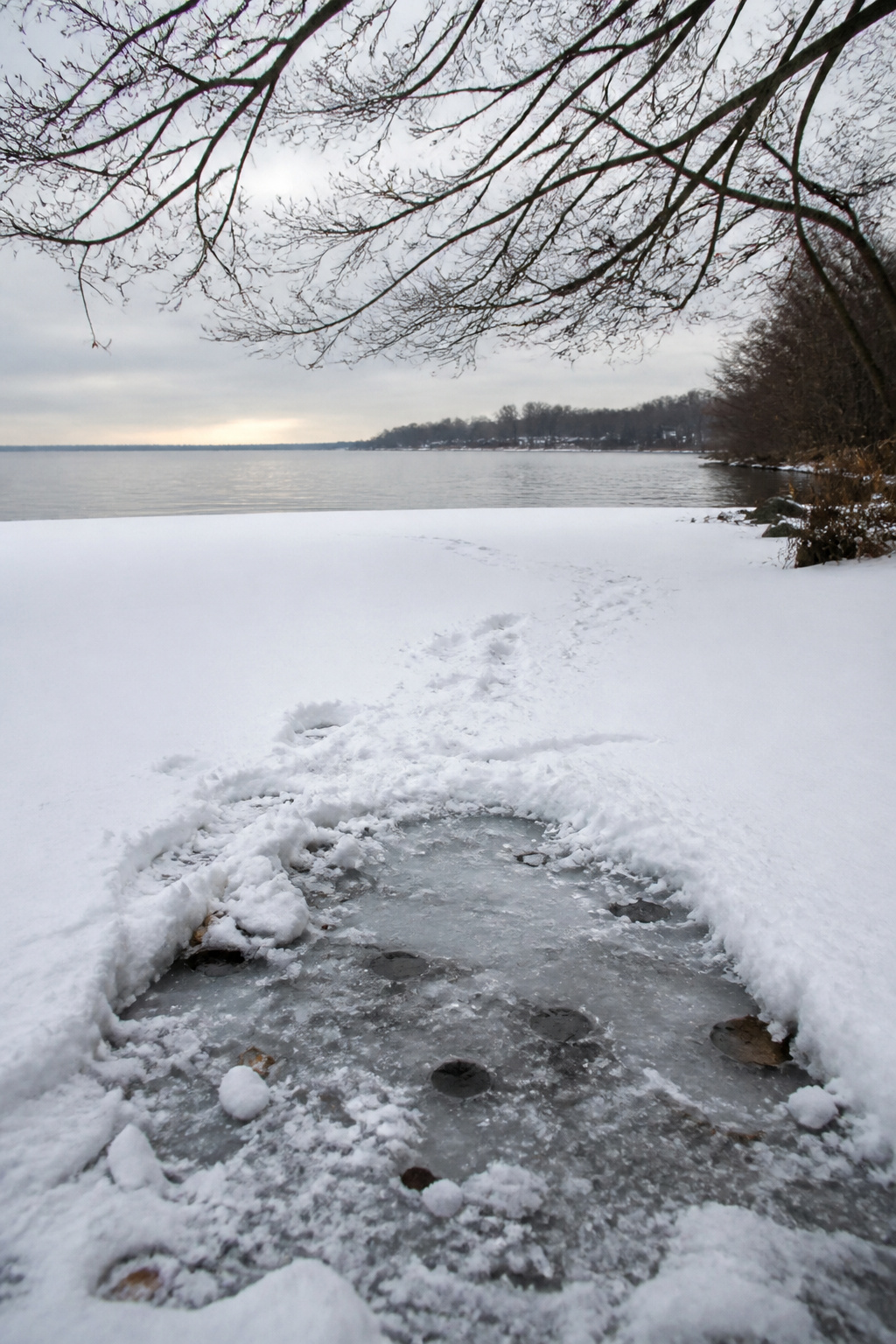 A thick layer of snow atop a frozen lake with disturbed snow in the foreground.