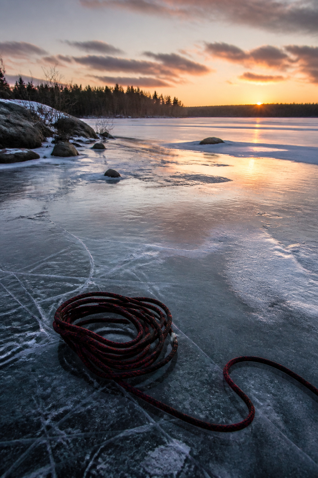 A frozen lake at sunset with a coiled rope lying on the ice.