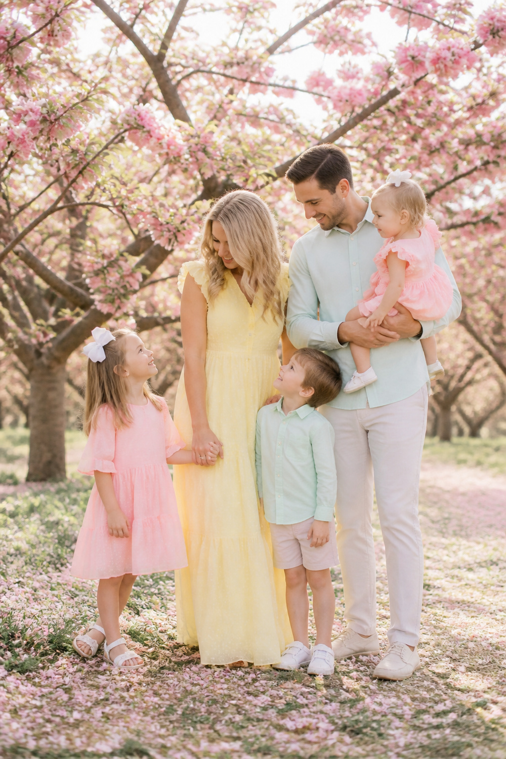 7 Spring Family Pictures Outfit Ideas for 2026 5 Family dressed in pastel colors poses in front of flowering trees.